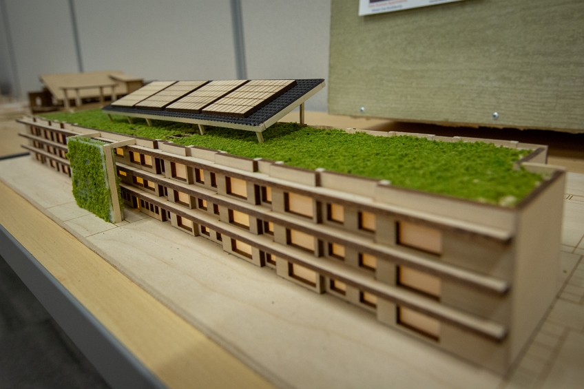 Photo of a wooden model from the 2019 Design Challenge. The model building appears to have solar panels on the roof as well as grassy areas.