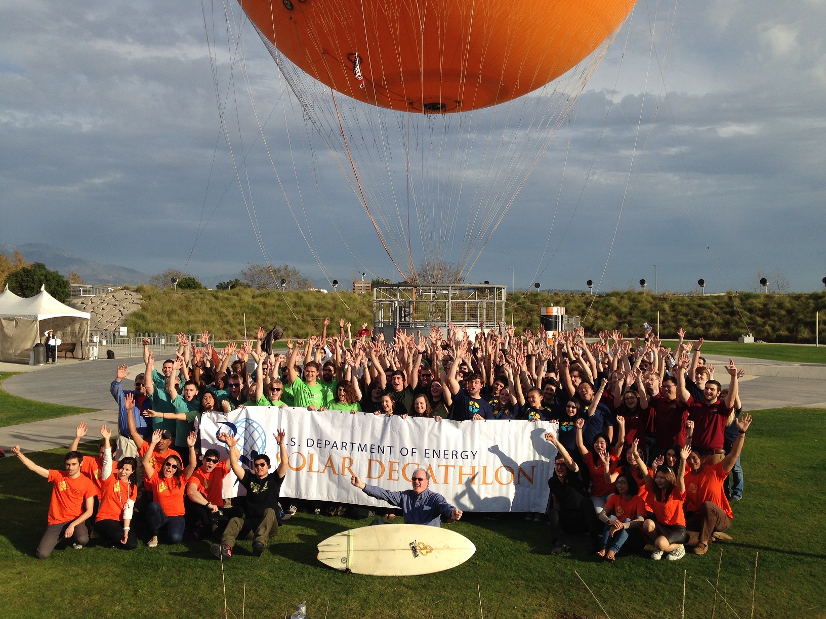 Photo of a large group of cheering people in front of a balloon and holding a banner that reads, “U.S. Department of Energy Solar Decathlon.”