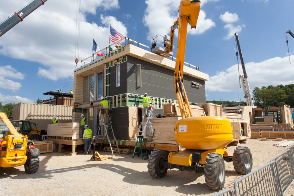 Photo of a partially constructed house with two stories and French and U.S. flags waving on the roof.