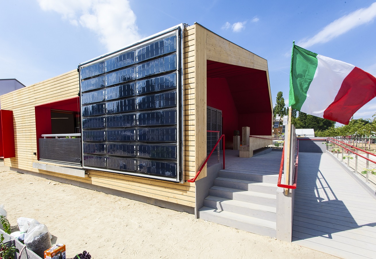 Photo of a modern house with solar PV panels on its side and an Italian flag near the front entrance.