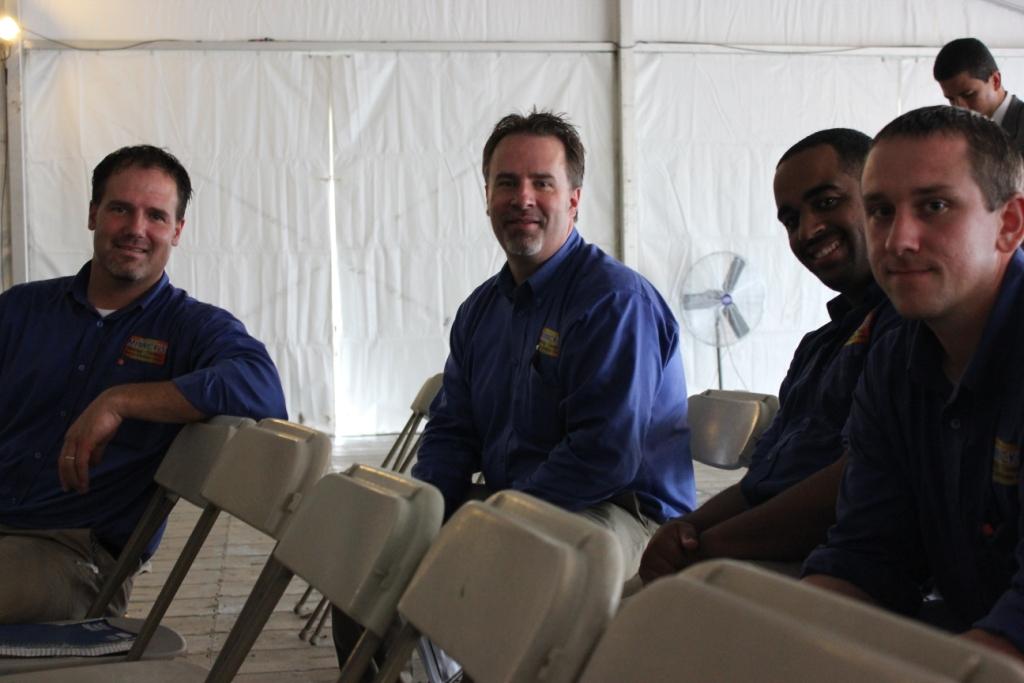 Photo of four men sitting in folding chairs inside a tent.