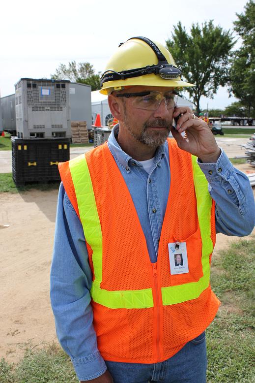 Photo of a man wearing a hard hat, safety glasses, and safety vest and talking on a mobile phone.