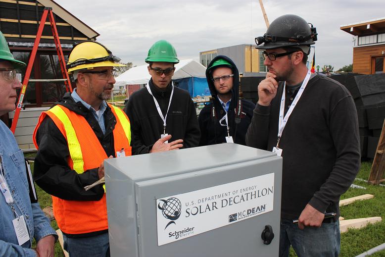 Photo of men in hard hats standing around an organizer utility panel.
