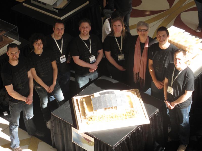 Photo of a group of people standing around a small table with a model of TRTL.