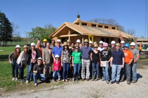 Photo of a group of people wearing hardhats in front of a partially constructed house. 