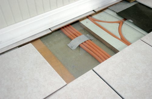 Photo of a section of tiled floor that has been removed to reveal radiant heating tubes below.