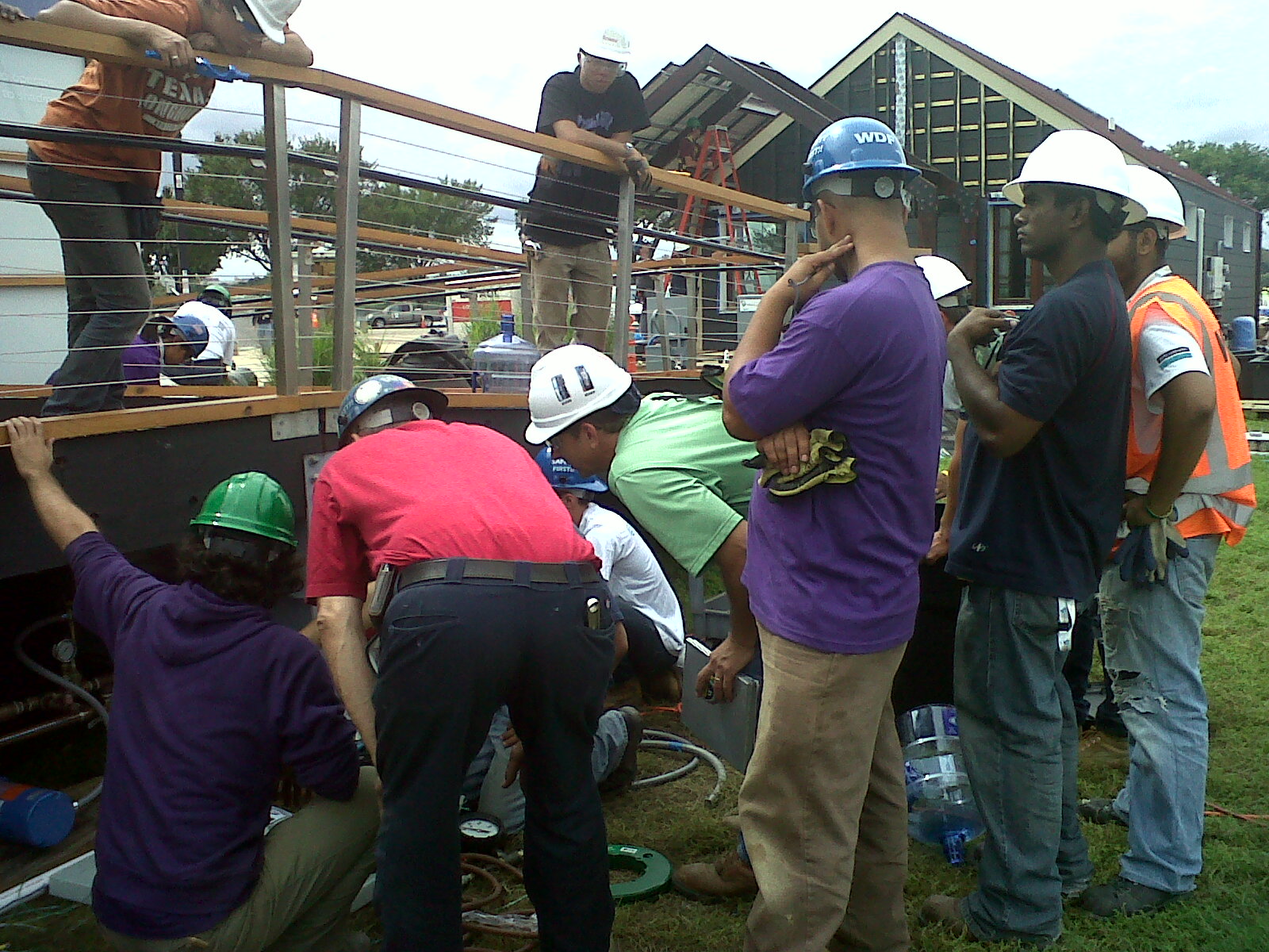 Photo of team members surrounding the building inspector as he looks underneath the deck of a house.