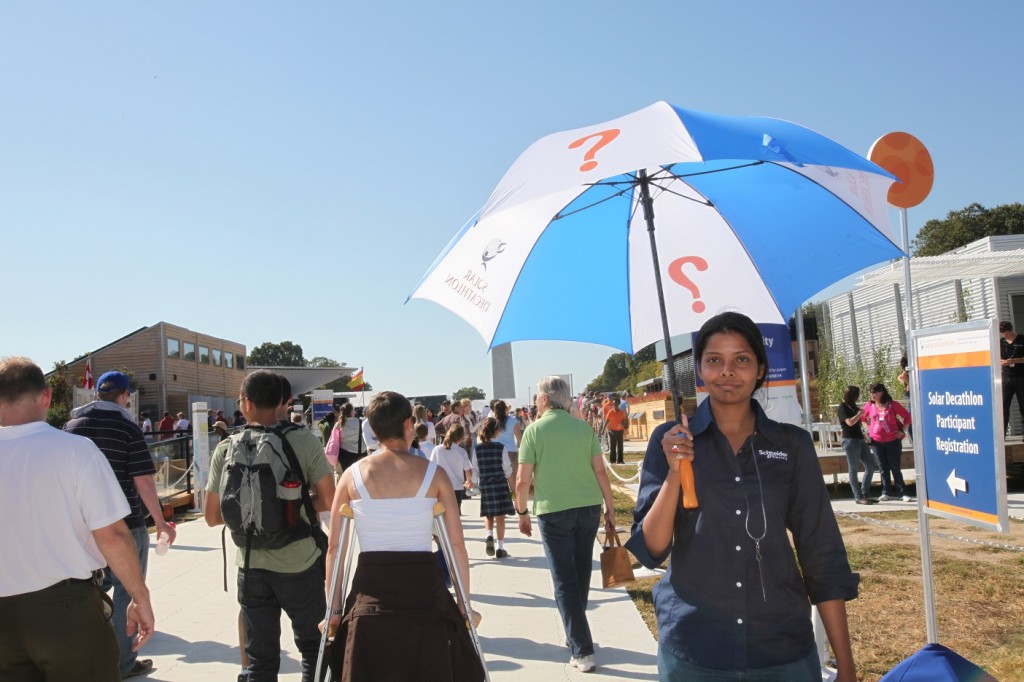 Photo of a volunteer holding an umbrella printed with a question mark in the Solar Decathlon village.