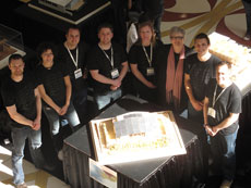 Photo of a group of people wearing matching black t-shirts and standing around a model of TRTL.