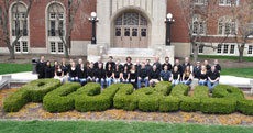 Photo of the Purdue University team members in front of a building on campus. In front of them is a hedge cut to read "Purdue."