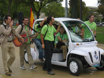 Photo of people driving electric vehicle and people with a guitar and flute walking beside the car.