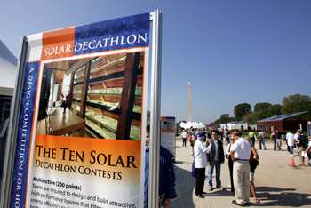 Photo of a banner about the Solar Decathlon, with solar village and visitors to the National Mall in background.