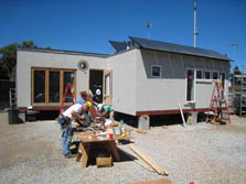 Photo of team members bent over a workbench in front of their Solar Decathlon house.