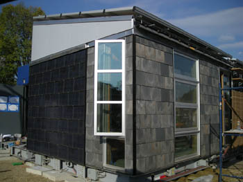 Photo of a house with slate tiles on one side and part of another, then darker tiles with horizontal lines in them, suggesting they are made of photovoltaic materials.