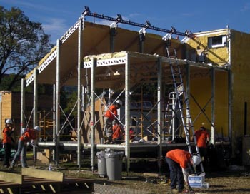 Photo of a solar house showing metal framework; four team members are standing on the ground.