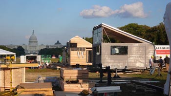 Photo of construction in the solar village on the National Mall. On the right are two unfinished houses. In the background is the U.S. Capitol.