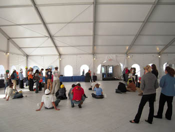 Photo of the inside of a large white tent, with student decathletes standing in a wide circle wearing hard hats. A speaker stands at a podium in the background.