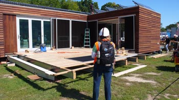 Photo of a woman with her back to the camera in front of a partially completed deck on the front of a house.