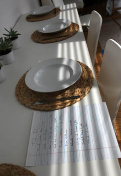 Photo of a long table set with dinner place settings. In the foreground is a to-do list written on notebook paper.