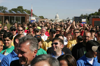 Photo of a large group of students, many of whom are clapping their hand above their heads. In the background is the U.S. Capitol.