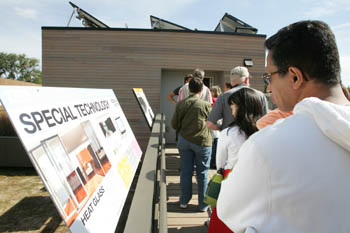 Photo of a line of people on the ramp of a house. On the left is a series of educational signs.