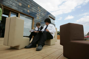 Photo of two children sitting on a small couch on the deck of Team Germany's house and writing on papers in their laps.