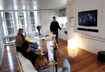 Photo of four students inside a house. A movie is playing on a TV in the living area.