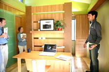 Two jurors holding notebooks listen intently as a young member of the Lawrence Technological Team explains the home's environmental features and sustainable materials during the 2007 Solar Decathlon. Between them is a desk and chair made from sustainable wood.