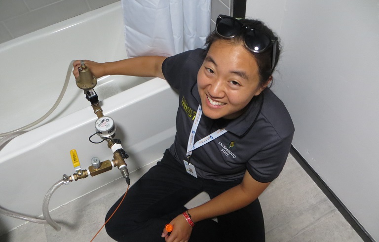 Photograph of a woman sitting on the floor next to a bathtub handling equipment that gauges water volume.