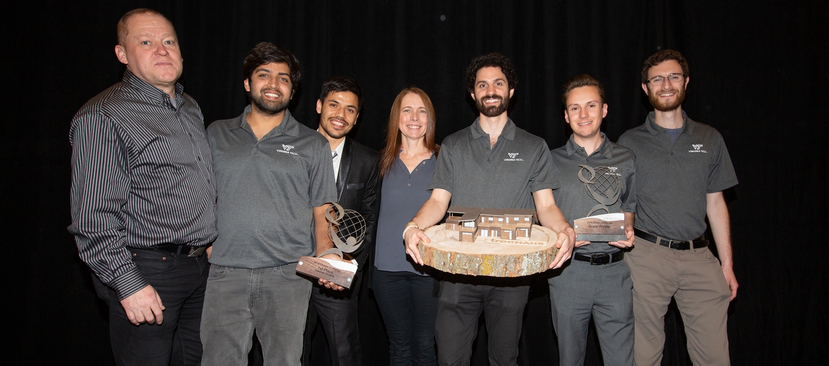 Photo of the winners of the 2019 Design Challenge. There are seven individuals posing with two trophies and a model of their winning design.