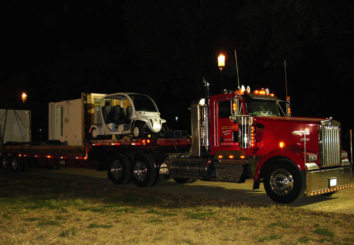 Photo of a semi-truck carrying an electric car and parts of a Solar Decathlon team house.