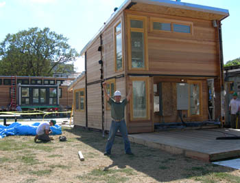 Photo of a smiling New York Institute of technology student standing in front of his Solar decathlon solar house on the National mall. His hands are raised above his head in excitement.