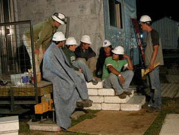 Photo of seven students in hard hats sitting on stairs.