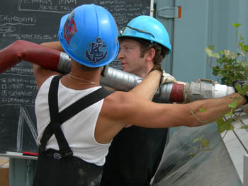 Photo of two men lifting a large water hose.