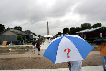 Photo of a man visiting the Solar Decathlon and holding a blue and white umbrella imprinted with a large question mark. 