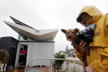 Photo of a man in a raincoat carrying a wet dog at the Solar Decathlon.