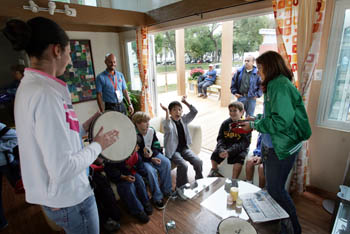Photo of children, inside a home, clapping along to a tambourine player.