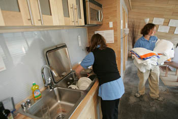 Photo of a student loading a dishwasher and another holding folded towels.