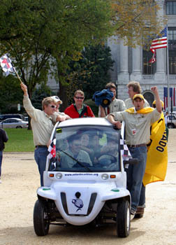 Photo of students driving and students standing on the runner boards of an electric vehicle.