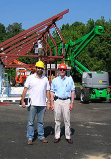 Photo of Richard King and Sergio Vega, wearing hardhats and standing in front of the frame of the Madrid Solar Decathlon house.