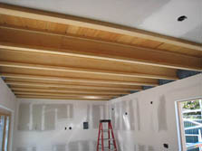 Photo of a dry walled room with a ladder on one end and a view of the ceiling joists.