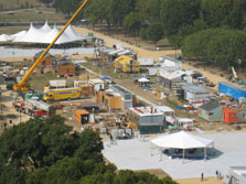 An aerial view of the west end of the Solar Decathlon includes ten partially completed houses, a large crane, and two tents.