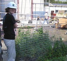 Photo of a young woman with a hard hat working on wire frames that have green vines growing on them.