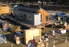 An aerial view, looking down on one house under construction with piles of wood, panels, and other materials and equipment lying on the ground.