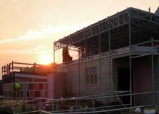 Photo of the sun rising just over the top of a solar house under construction.