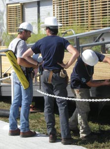 Photo of three men in hard hats gathered around a ramp leading to the front of a solar home.