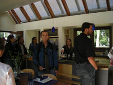 Photo of several people standing inside a house with a dining room table in the foreground and a kitchen in the background.