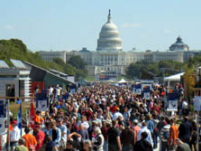 Photo of a dense crowd of people lining the walkway between the houses on the solar village, with the U.S. Capitol building in the background.