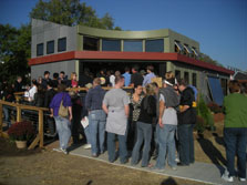 Photo of a crowd of about 30 people standing in a long line on a ramp leading up to the front of a house.