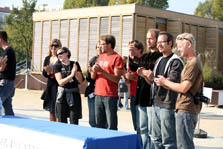 Photo of an outdoor scene with nine people standing behind a table.
